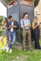grupp av raser vänner i främre av en tidningskiosk använder sig av smartphones foto
