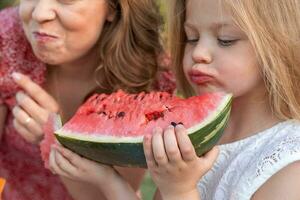 porträtt av mamma med söt döttrar ha roligt medan äter en skiva av vattenmelon foto