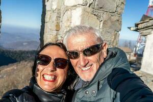 mitten åldrig par bär vinter- kläder tar en selfie över en berg foto