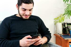 främre se av en Lycklig man använder sig av en mobil telefon på linje Sammanträde på en soffa foto