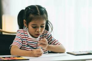 asiatisk liten flicka teckning med pennor på Hem. utbildning begrepp. foto