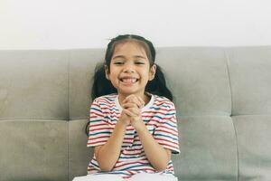 söt asiatisk barn flicka Sammanträde på soffa på Hem och leende foto