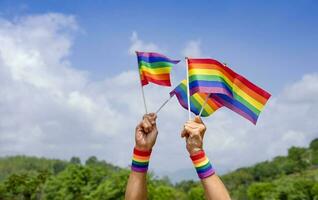 människor hand innehav HBTQ färgrik regnbåge Gay flagga bakgrund blå himmel på sommar, koncept av lgbtq mångfald kön kärlek, aktivist, rättigheter, protest, rörelse parad, fira, festival, Lycklig stolthet månad foto