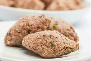 steg förbi steg levantin kök kibbeh förberedelse. rå kibbeh bollar på vit maträtt foto