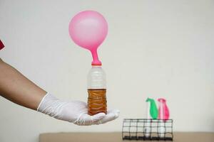 hand innehar rosa uppblåst ballonger på topp av transparent testa flaskor med mjuk dryck blanda bakning soda. begrepp, vetenskap experimentera handla om reaktion av kemisk ämne. foto