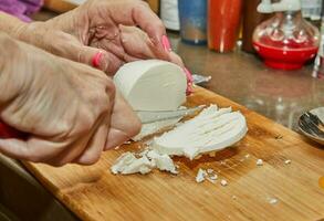 kock nedskärningar de ost med kniv på trä- styrelse för framställning en paj foto