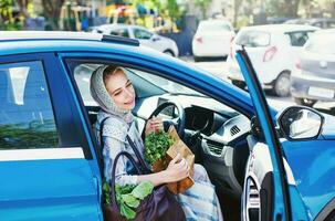 muslim kvinna i en blå bil med en handla väska foto