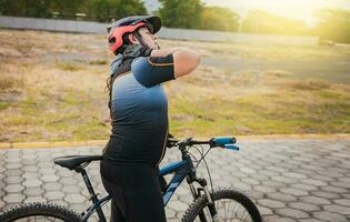 sportig cyklist har nacke smärta medan ridning en cykel. manlig cyklist med nacke smärta utomhus foto