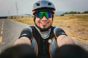 själv porträtt av Lycklig manlig cyklist utomhus. Lycklig cyklist med glasögon och hjälm tar en selfie foto