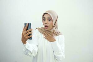 upphetsad skön asiatisk muslim kvinna som visar mobil telefon isolerat över vit bakgrund foto