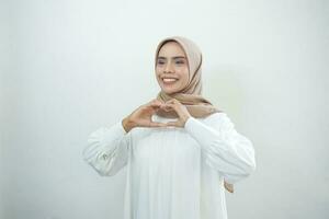porträtt av leende asiatisk muslim kvinna som visar hjärta gest isolerat över vit bakgrund foto