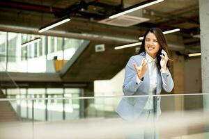 ung företag kvinna använder sig av mobil telefon i de kontor hall foto