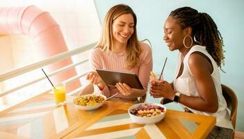 ung svart och caucasian kvinna har Bra tid, dricka färsk juicer och har friska frukost i de Kafé foto