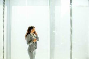 ung kvinna använder sig av mobil telefon förbi de kontor fönster foto