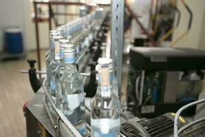en rad av glas flaskor på en transportband bälte för de produktion av alkoholhaltig drycker. foto
