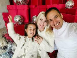 familj, högtider, teknologi och människor - leende mor, far och liten flicka framställning selfie med kamera över levande rum och jul träd bakgrund foto