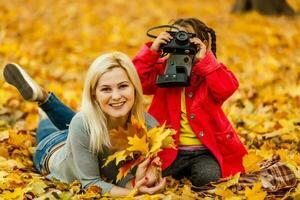 liten flicka spelar med en kamera i gul löv av höst landskap foto