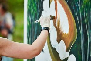 flicka konstnär hand innehar måla borsta och drar grön natur landskap på duk foto