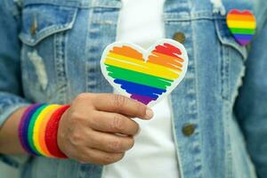 asiatisk dam som bär regnbågsflaggarmband och håller rött hjärta, symbol för HBT stolthet månad firar årliga i juni sociala av homosexuella, lesbiska, bisexuella, transpersoner, mänskliga rättigheter. foto