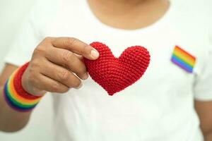 asiatisk lady bär regnbåge flagga armband och håll hjärta, symbol av HBTQ stolthet månad fira årlig i juni social av Gay, lesbisk, bisexuell, transpersoner, mänsklig rättigheter. foto