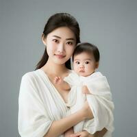 ung kvinna innehav bebis i vit skjorta på grå bakgrund foto