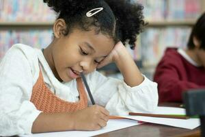 skola klass porträtt av en lysande svart flicka med tandställning skrivningar i övning anteckningsbok, ler. junior klassrum barn inlärning ny grejer foto