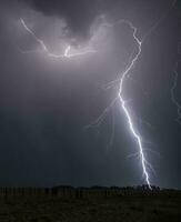 blixt- strejker över en fält i de mörk himmel foto