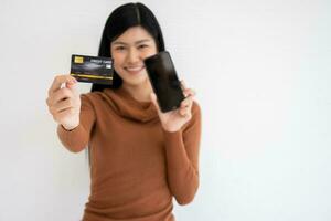 Lycklig asiatisk kvinna innehav kort kreditera och smartphone för mobil bank på de internet. begrepp av ny livsstil och finansiering teknologi. foto