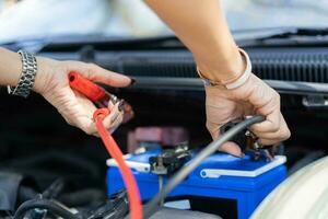 stänga upp och selektiv fokus av bil mekaniker innehav batteri elektricitet kablar hoppare för laddning bil batteri, tjänster bil motor maskin begrepp foto