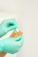 kosmetolog i grön skyddande handskar innehar en hantverk kuvert till sterilisera verktyg innan desinfektion. foto