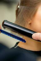 en frisör är rätning de hår av de ung brunett kvinna i en skönhet salong. foto
