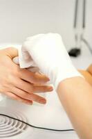 händer av en manikyrist i vit skyddande handskar torka kvinna naglar med en papper servett i de salong. foto