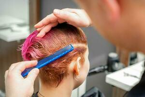 kammande de hår av en ung kvinna under färg hår i rosa Färg på en hår salong stänga upp. foto