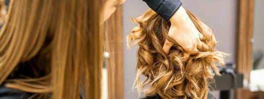 kvinna frisör checkar brun lockigt frisyr av en ung caucasian kvinna i skönhet salong. foto