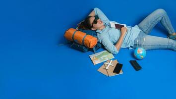 turistplaneringssemester med hjälp av världskartan med andra resetillbehör runt om. kvinna resenär sover koppla av i handen håller en biljett med ett pass på blå bakgrund. reseryggsäck foto