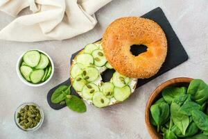 utsökt bagel fylld med feta, gurka och pumpa frön och spenat löv på en skiffer styrelse. ljus vitamin friska mellanmål. topp se foto