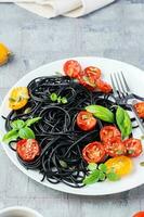 aptitlig svart spaghetti med torkades tomater, pumpa frön och sesam frön på en vit tallrik på de tabell. gourmet mat. vertikal se. närbild foto