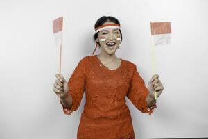 Lycklig leende indonesiska kvinna bär röd kebaya och pannband innehav Indonesiens flagga till fira indonesien oberoende dag isolerat över vit bakgrund. foto