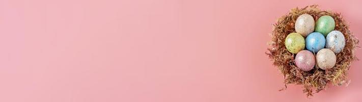 påskägg i ett naturligt rede med mossa på en rosa bakgrund. vy från ovan. baner foto