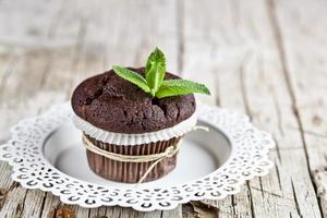 färsk mörk chokladmuffin med mynta lämnar på den vita plattan på rustikt träbord. foto