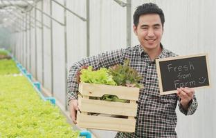 asiatisk man som håller en korg med färska grönsaker och ekologiska grönsaker från gårdens grönsaksodling och hydroponics hälsokoncept för jordbruk foto