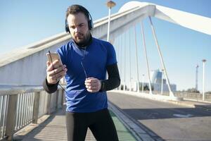 en närbild skott av en manlig i blå hörlurar använder sig av hans mobil medan joggning i de gata foto