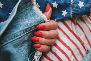 skön kvinna händer med en ljus röd matt manikyr på de bakgrund av jeans. eleganta oval nagel design, amerikan stil. sommar manikyr. kopia Plats. foto
