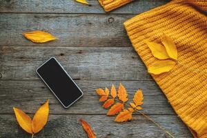 smartphone, höst löv och stickat orange Tröja på en trä- bakgrund. höst begrepp. se från ovan foto