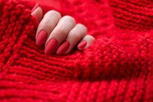 kvinnors händer med en skön matt oval manikyr i en värma röd stickat Tröja. vinter- trend, omslag röd naglar med gel putsa, schellack. foto