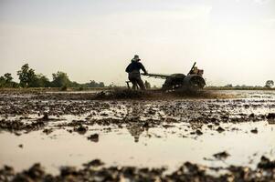 låg vinkel se, jordbrukare är körning gå-bakom traktor till plog vattenfylld grumlig jord. foto