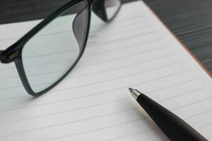 en penna, bok och solglasögon placerad på en texturerad tabell, efter några redigeringar. foto