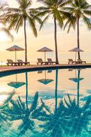vackert lyxigt paraply och stol runt utomhuspoolen på hotellet och resort med kokospalmer på solnedgången eller soluppgångshimlen