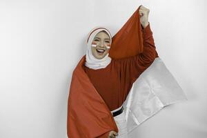 en ung asiatisk muslim kvinna med en Lycklig framgångsrik uttryck bär röd topp och vit hijab medan innehav Indonesiens flagga, isolerat förbi vit bakgrund. Indonesiens oberoende dag begrepp. foto