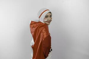 Lycklig leende indonesiska muslim kvinna bär röd topp och vit hijab innehav Indonesiens flagga till fira indonesien oberoende dag. isolerat förbi vit bakgrund. foto